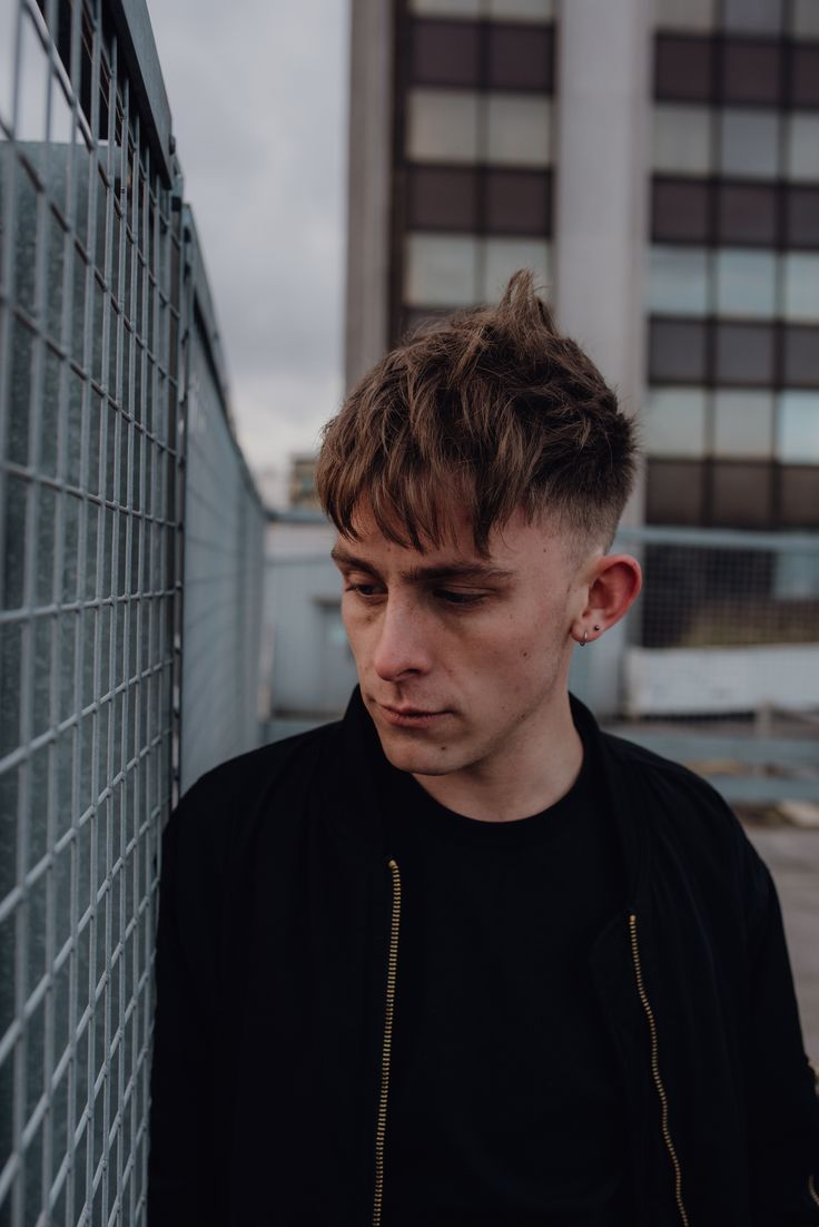 a young man leaning against a wall with his eyes closed and looking at the camera