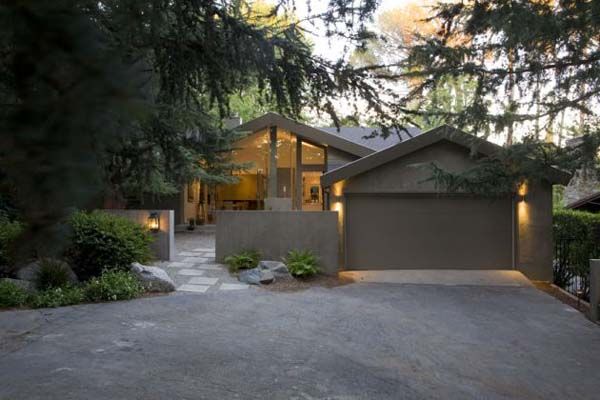 a house that is sitting in the middle of a driveway with trees and bushes around it