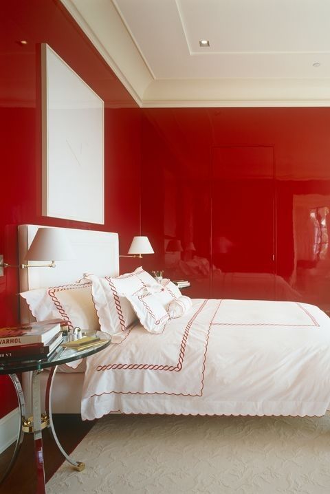 a bedroom with red walls and white bedding in the center, along with a glass side table