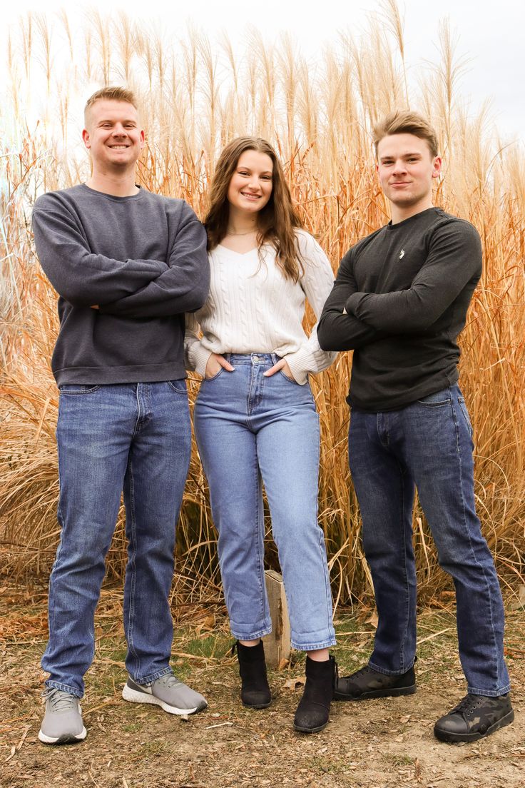 three people standing next to each other in front of tall grass