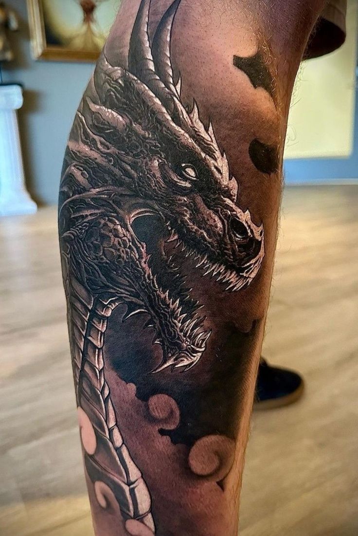 a man's leg with a black and grey dragon tattoo on the calf area