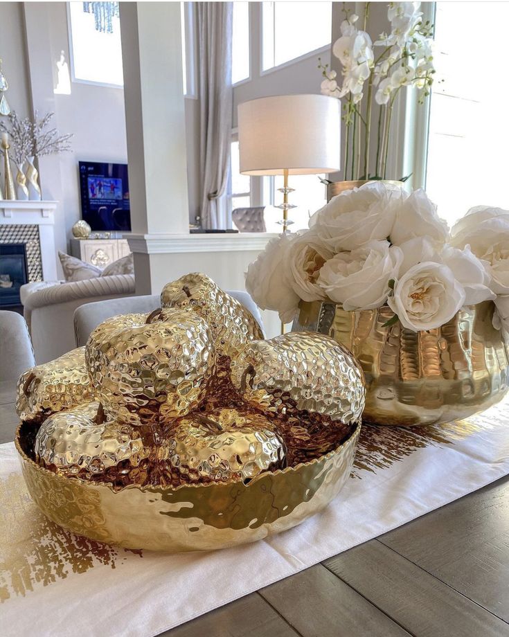 a table topped with two large gold bowls filled with flowers