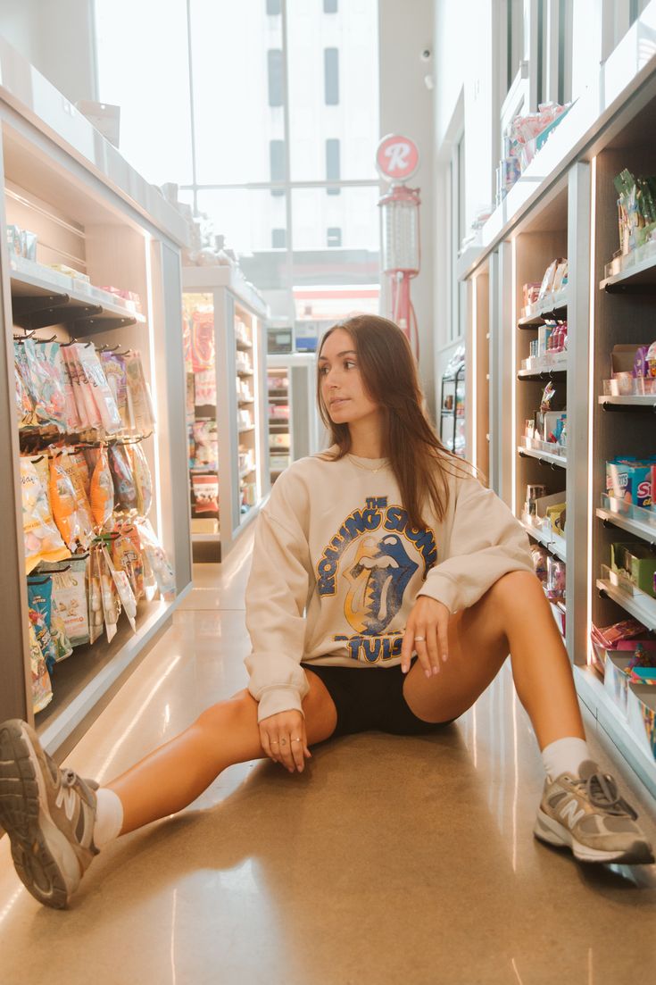 a woman sitting on the floor in front of a store shelf with her legs crossed