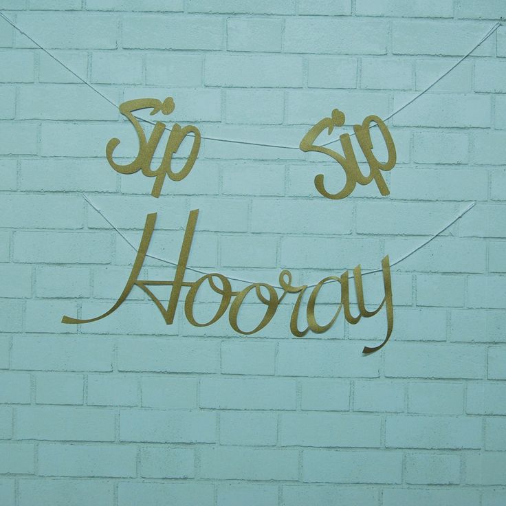 a sign that reads sip hooray hanging from a string on a brick wall