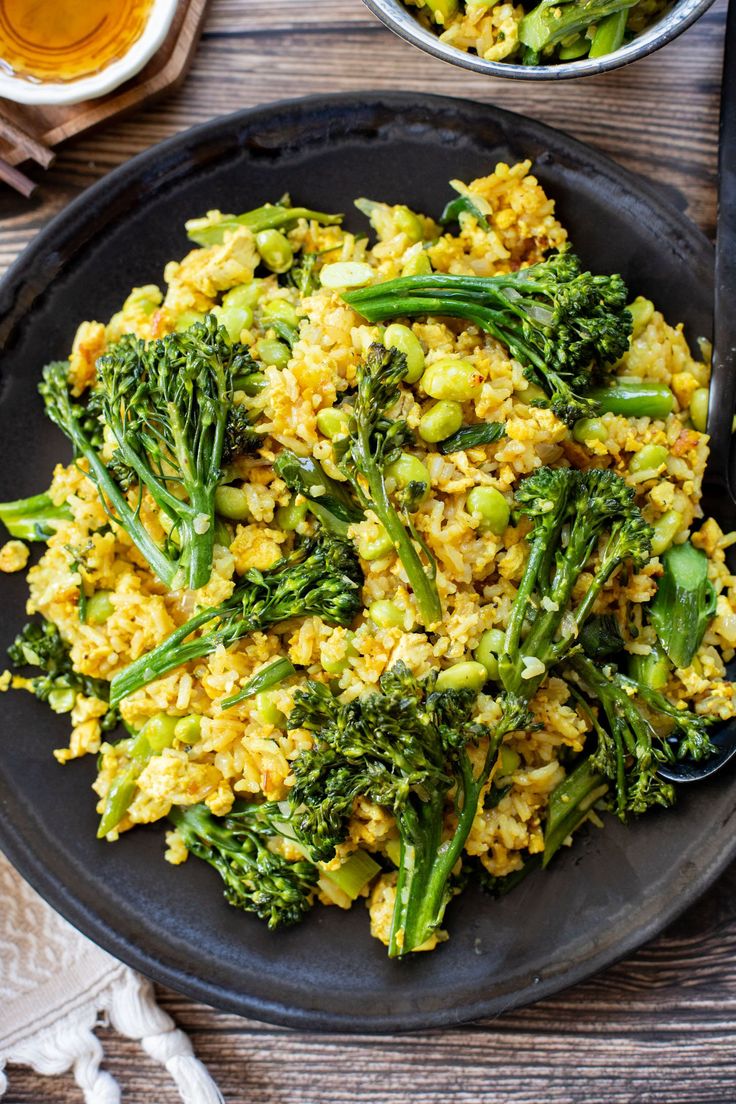 a black plate topped with rice and broccoli next to two bowls of food