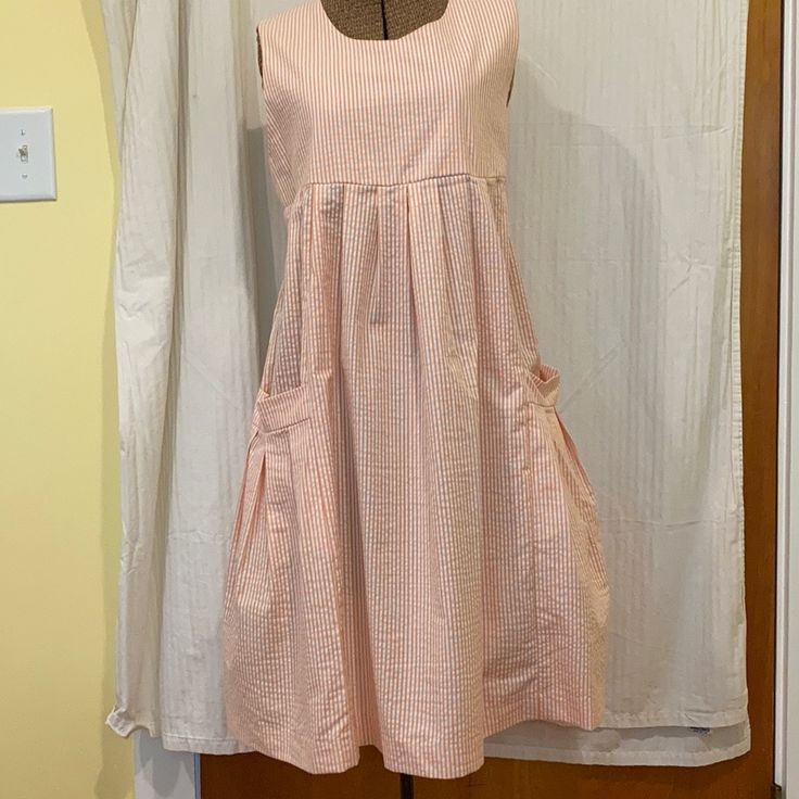 Sleeveless Sundress In Light Orange/Peach And White Seersucker. Pleated Around Slightly Empire Waistline, And Two Large Pockets. Cute White Buttons All The Way Down The Back. Bust Measures Approximately 36”, Length 36”. Nwot. Casual Striped Seersucker Dress, Sleeveless Seersucker Dresses For Daywear, Peach Sleeveless Cotton Dress, Sleeveless Peach Cotton Dress, Striped Sleeveless Seersucker Dress, Sleeveless Striped Seersucker Dress, Casual Seersucker Summer Dress, Casual Seersucker Dresses For Spring, Casual Fitted Seersucker Dress