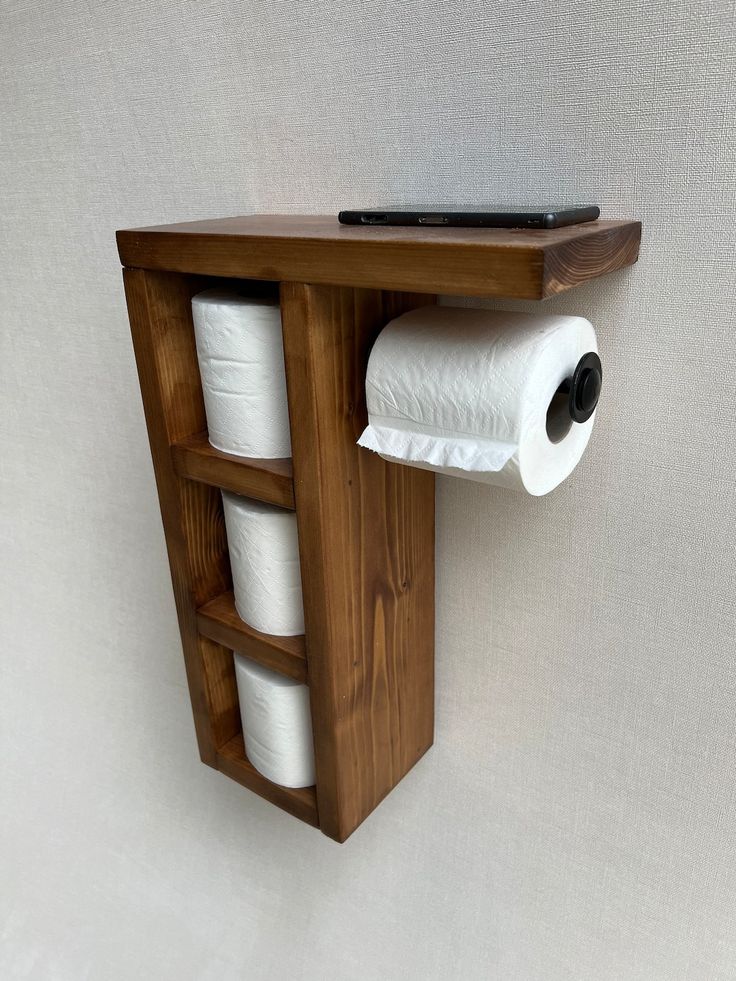 a wooden shelf with two rolls of toilet paper hanging on it's side and a laptop sitting on top