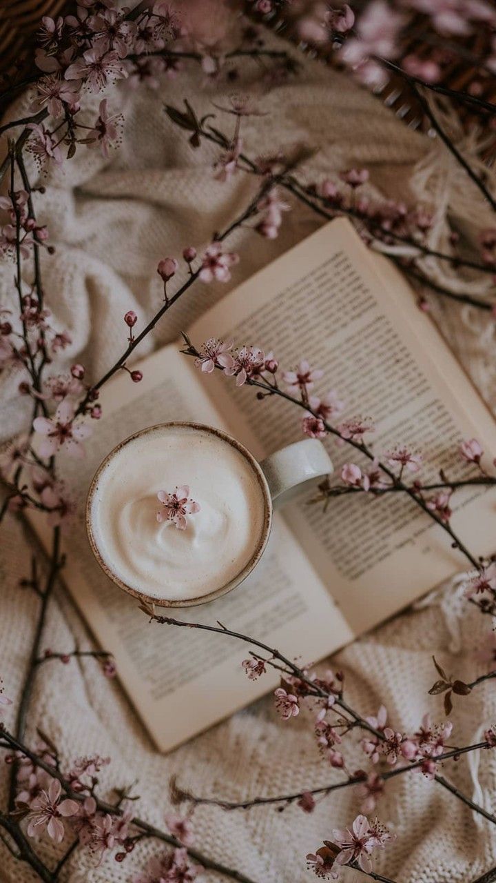 an open book on top of a blanket next to a cup of coffee and flowers