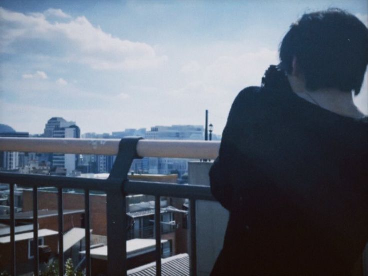 a woman standing on top of a balcony next to a metal railing with buildings in the background