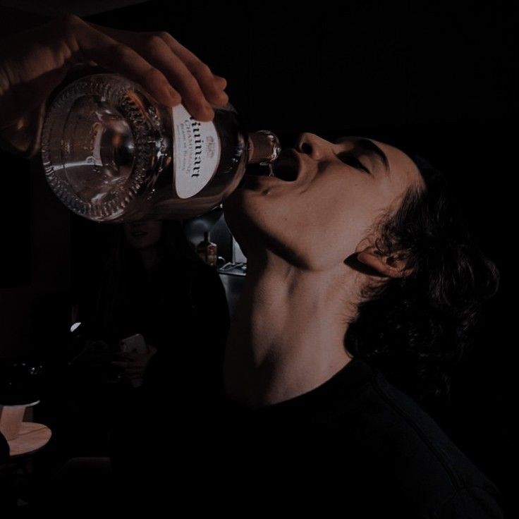 a man drinking from a bottle in the dark with his eyes closed and mouth wide open