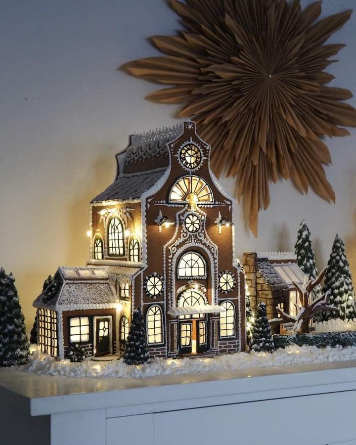 a lighted christmas house on top of a mantle with a star in the sky above it