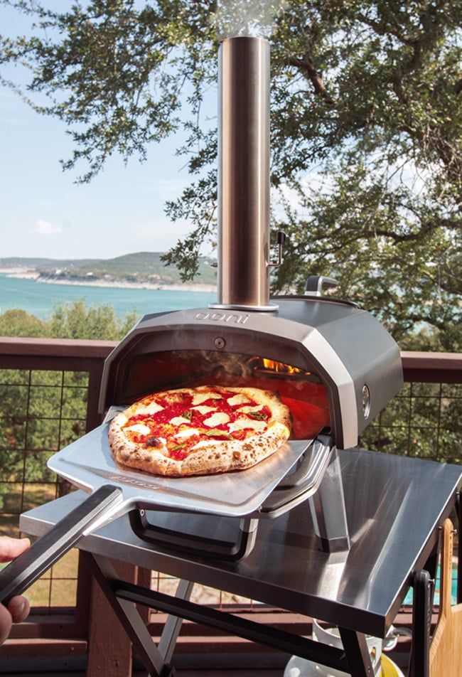 a pizza is being cooked in an outdoor oven on a deck overlooking the water and trees