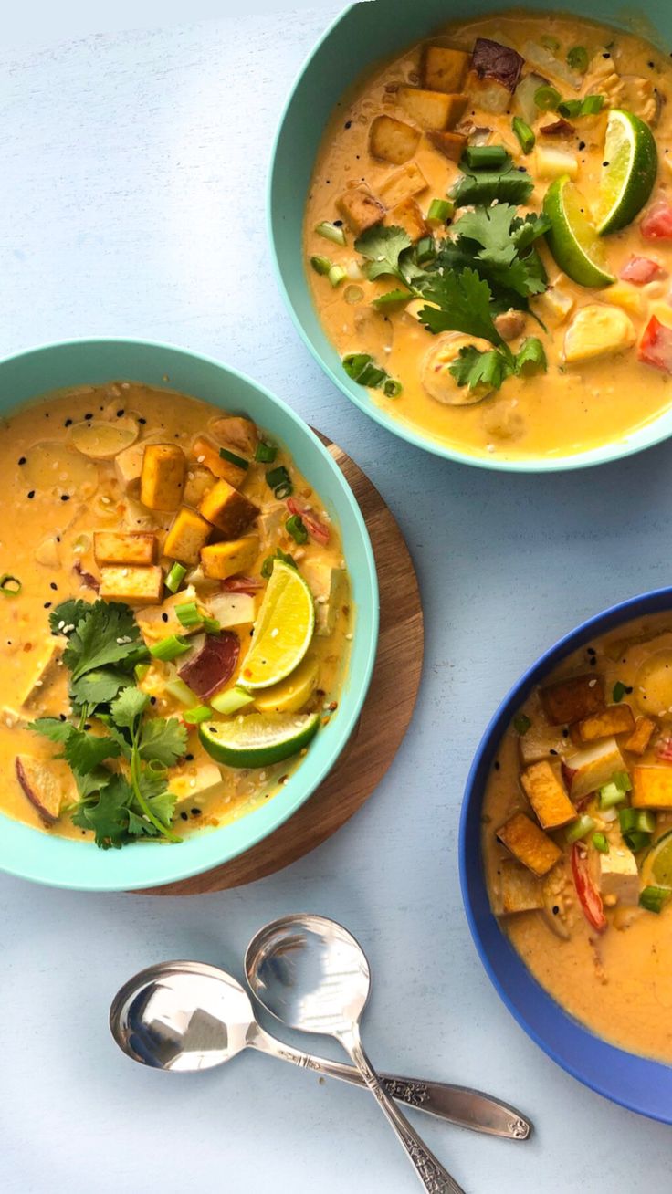 three bowls filled with soup next to spoons and silverware on a white surface