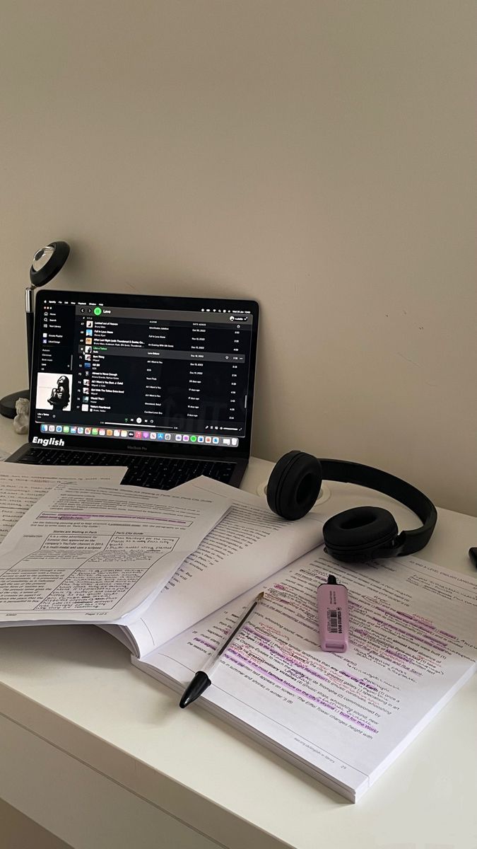 an open book sitting on top of a desk next to headphones and a laptop computer