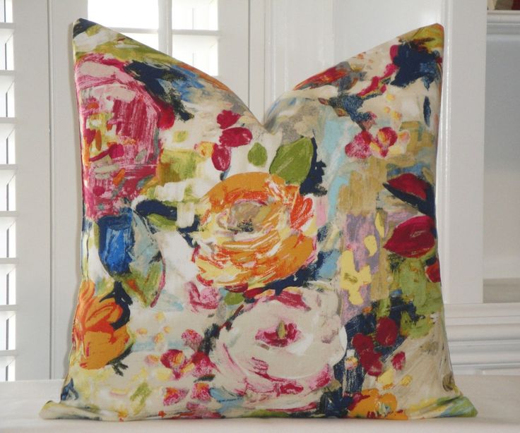 a colorful floral pillow sitting on top of a white couch next to a window with shutters