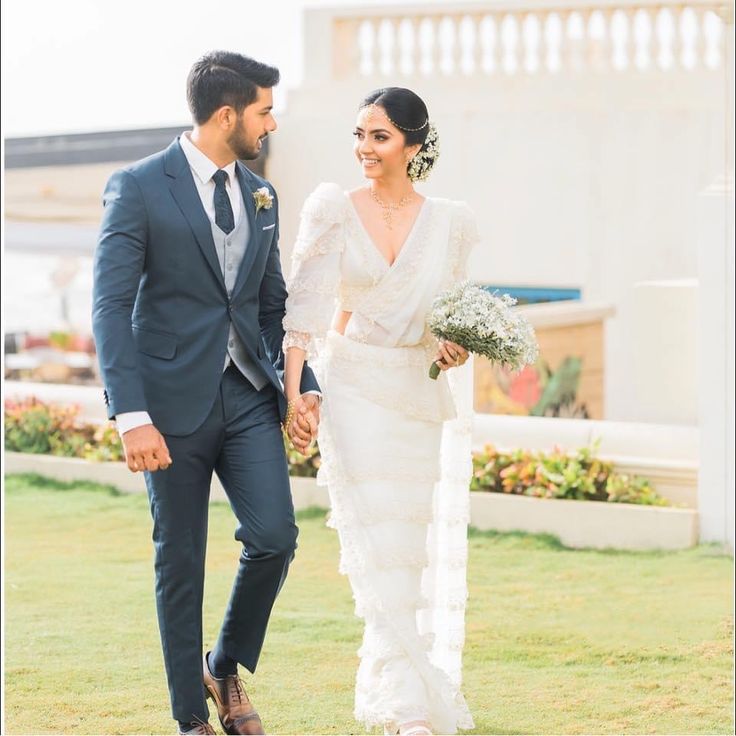 a bride and groom holding hands walking through the grass in front of a white building