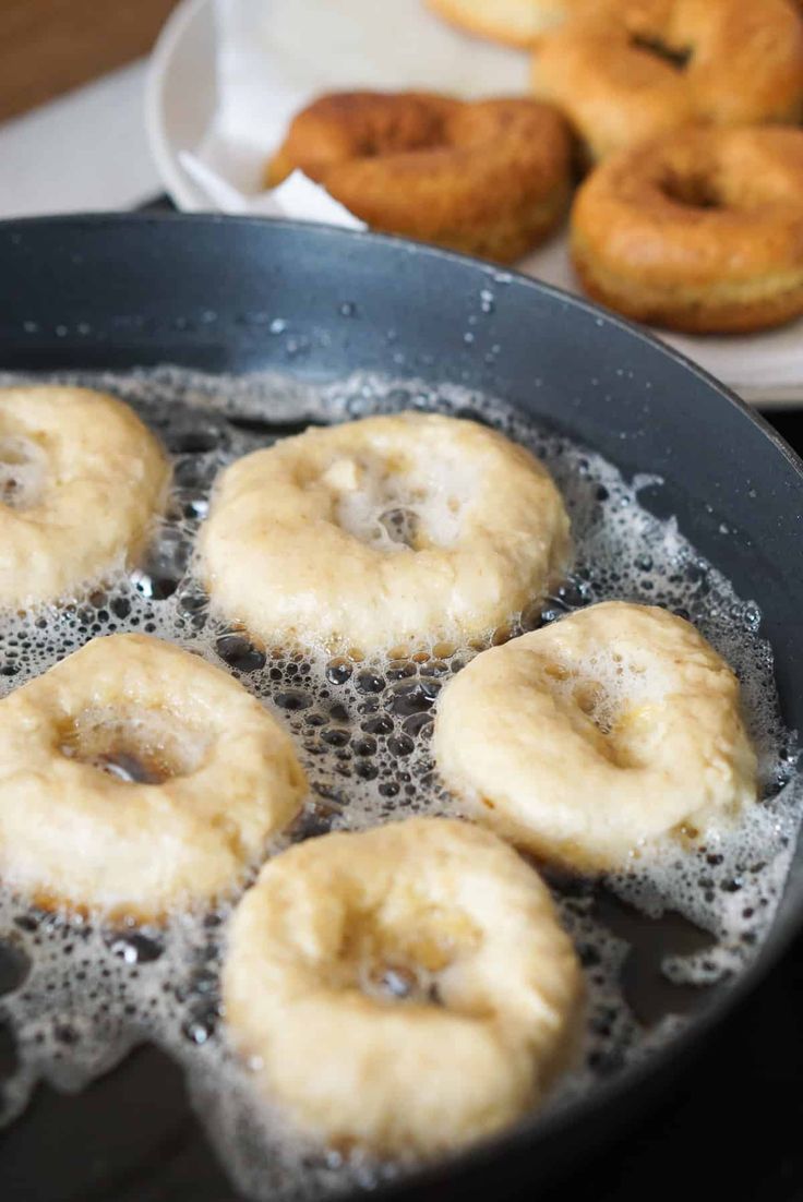 donuts frying in oil on a pan with other doughnuts behind it