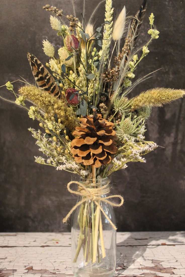 a glass vase filled with lots of different types of flowers and plants on top of a table