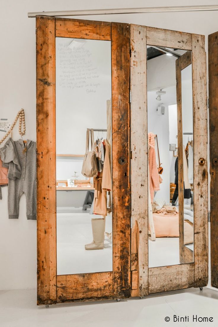 an open wooden door with clothes hanging on the wall and in front of it is a mirror