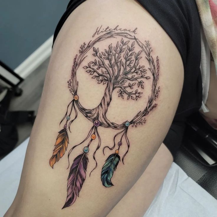 a woman's thigh with a tree and dream catcher tattoo on her left leg