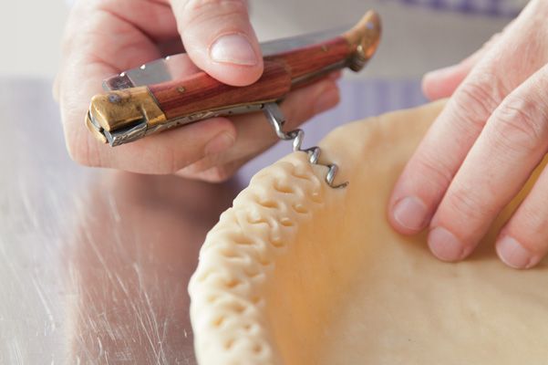 a person is using a small tool to cut out the top part of a pie