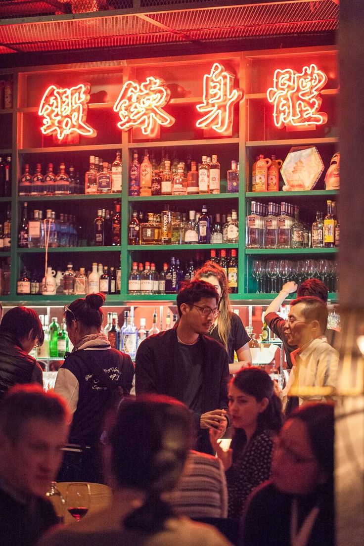 people sitting at tables in front of shelves with liquor bottles and neon signs on them