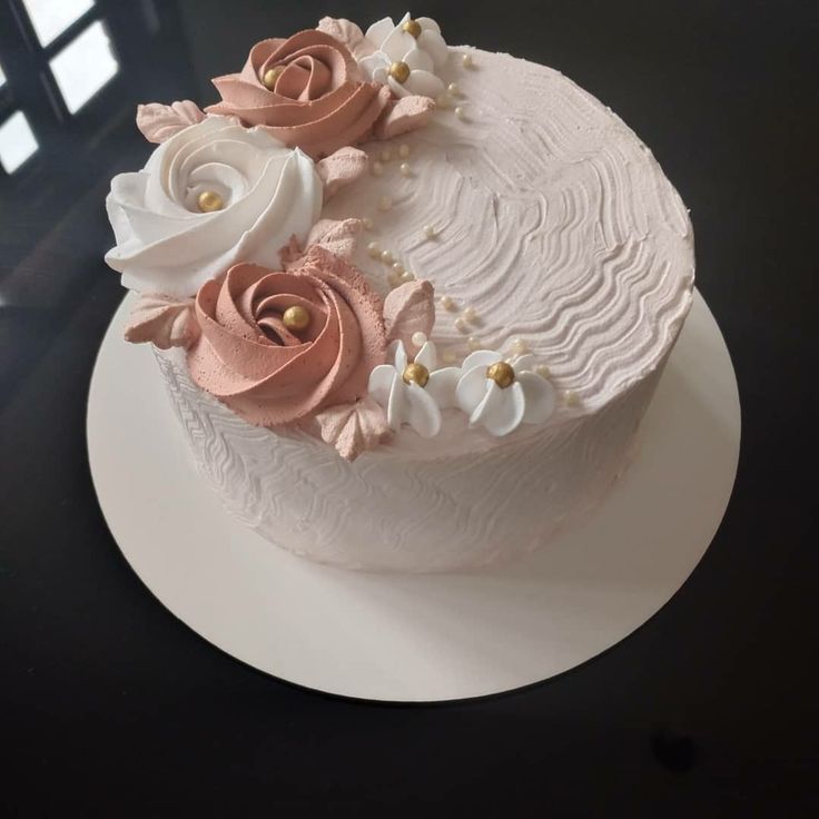 there is a white cake with pink and white flowers on the top, sitting on a black table