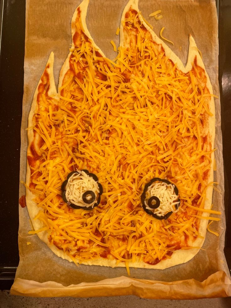 a pizza with cheese on it that looks like a fireball is in the shape of a face