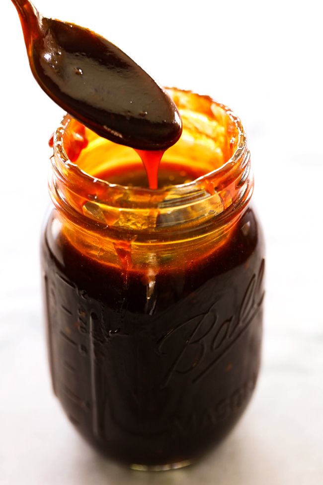 a spoon full of sauce on top of a jar filled with something orange and brown