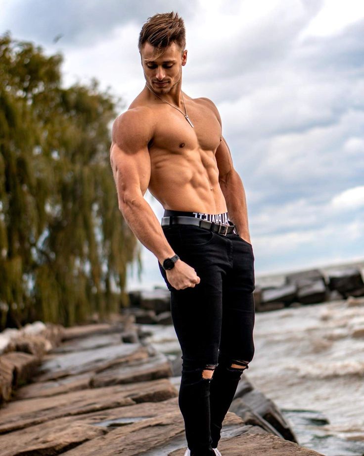 a shirtless man standing on rocks by the water