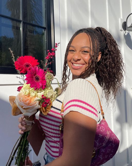 a woman is holding flowers and smiling for the camera while standing in front of a white building