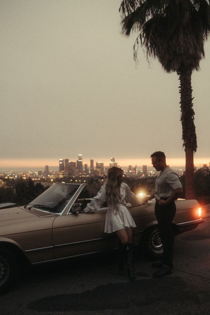 a man and woman standing next to a parked car in front of a cityscape