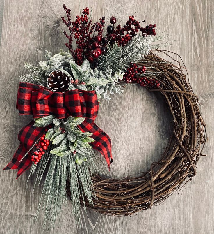 a christmas wreath with berries, pine cones and greenery on a wooden table top