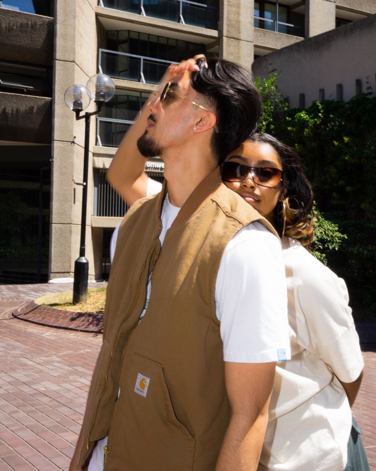 a man and woman walking in front of a building with sunglasses on their heads, one looking up at the sky