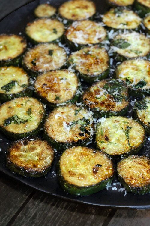 cooked zucchini on a black plate with parmesan cheese and seasoning