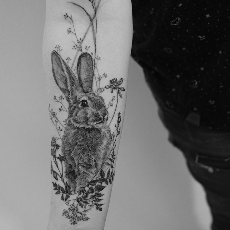 a black and white photo of a rabbit with flowers on it's arm,