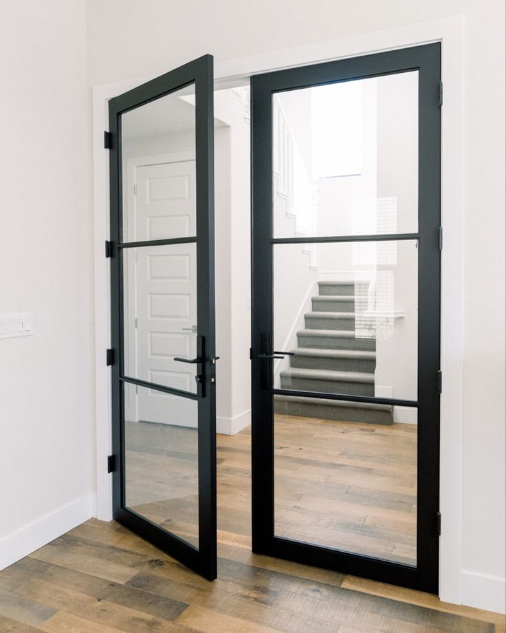 an empty room with two black doors and stairs in the background, looking into another room