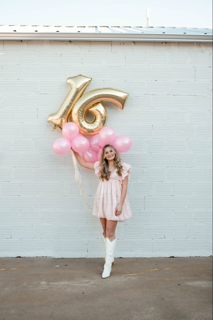 a girl in a pink dress and white boots is holding balloons with the number fifteen on it