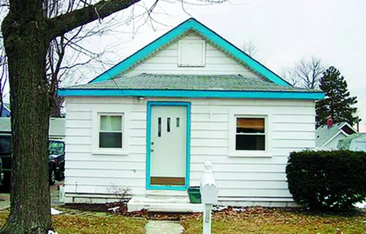 a small white house with blue trim on the front door and green trim on the windows