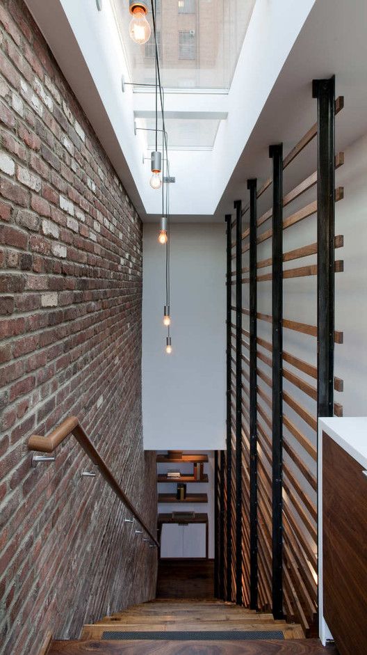 a long narrow hallway with brick walls and wooden steps leading up to an open skylight