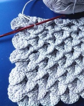 a crocheted dishcloth with yarn next to it on top of a blue table