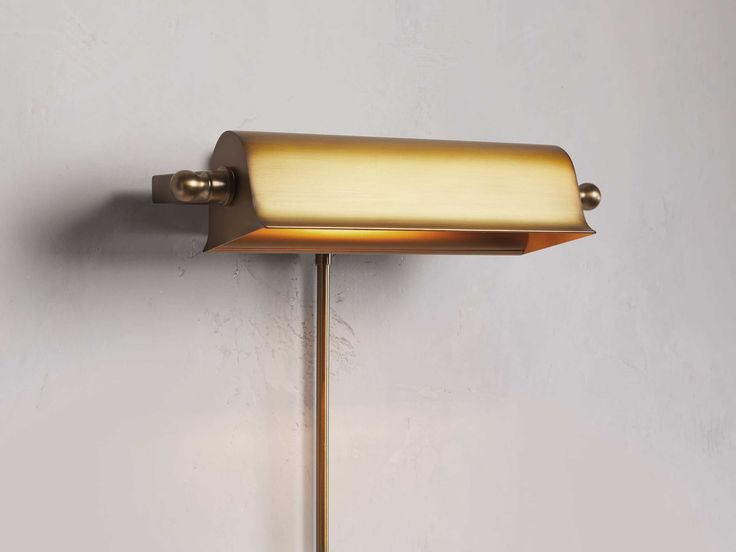 a wall light with a white background and a gold colored shade on the lamp fixture