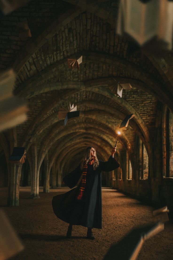 a woman in a long black coat is throwing papers into the air while standing under an archway