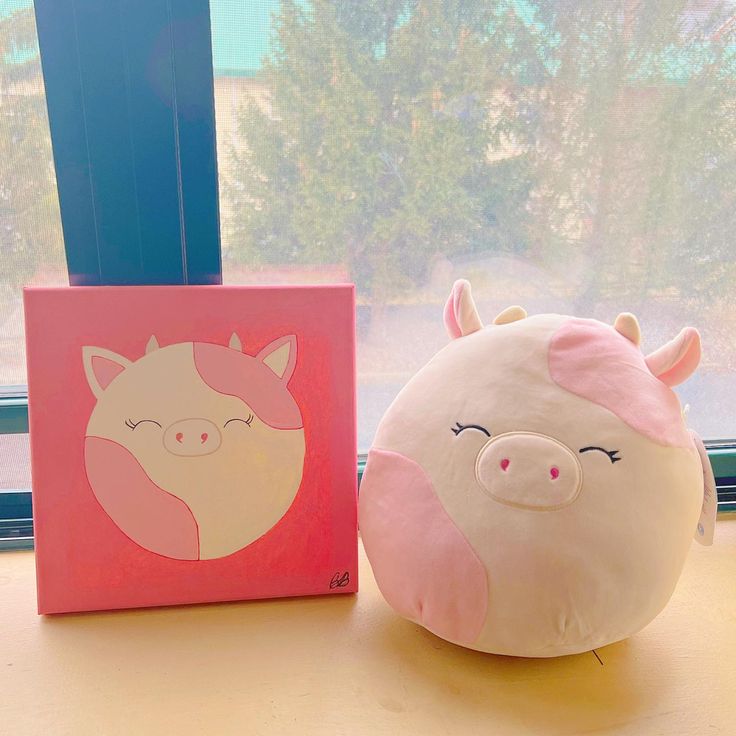 a stuffed pig sitting next to a window sill with a painting on it's side