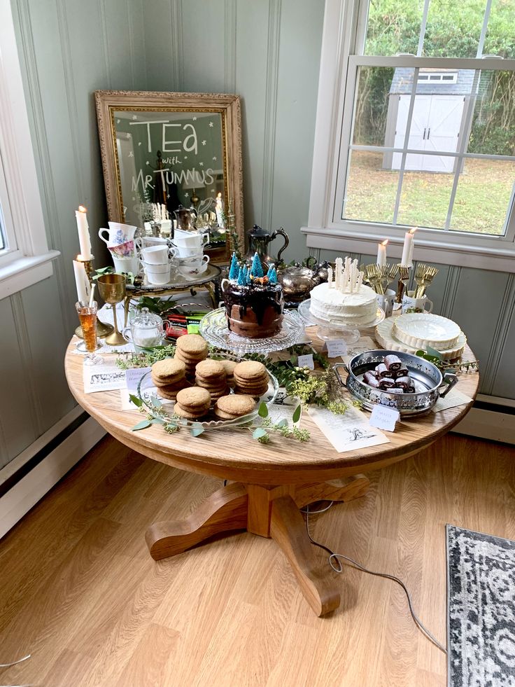 a table filled with cakes and pastries on top of a wooden floor next to a window