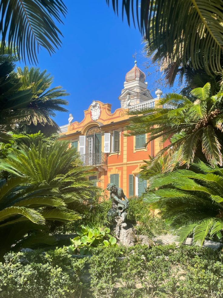 an orange building surrounded by palm trees and greenery with a clock on the top