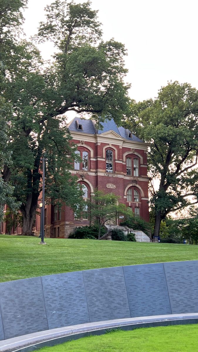 an old brick building in the middle of a grassy area with trees and benches around it