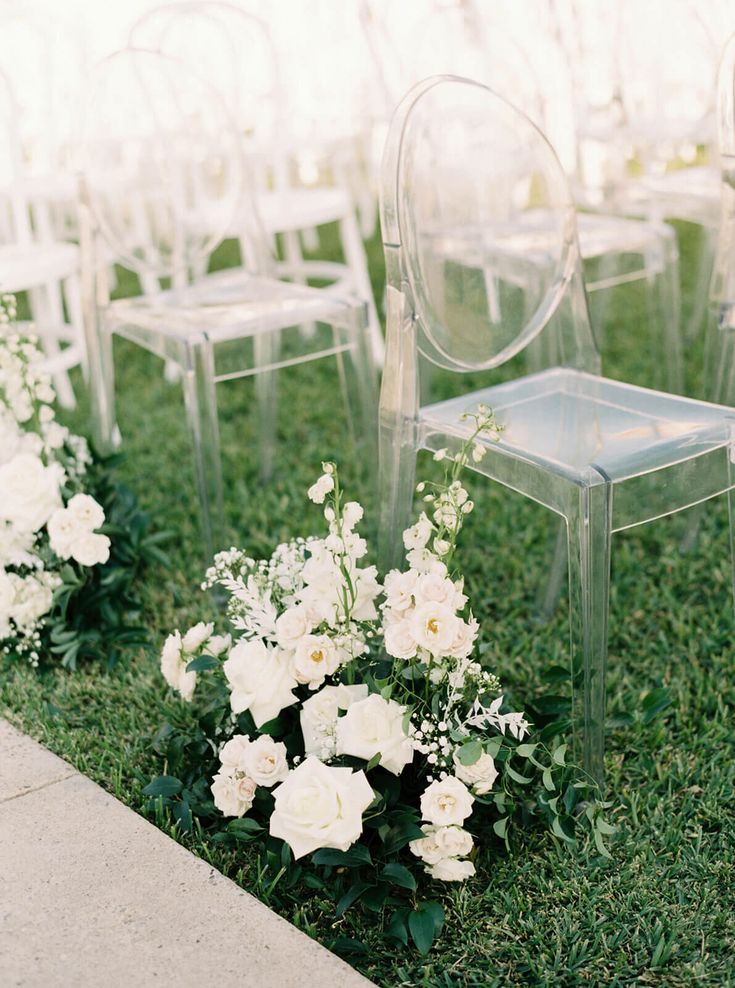 there are many clear chairs with white flowers in the grass next to eachother