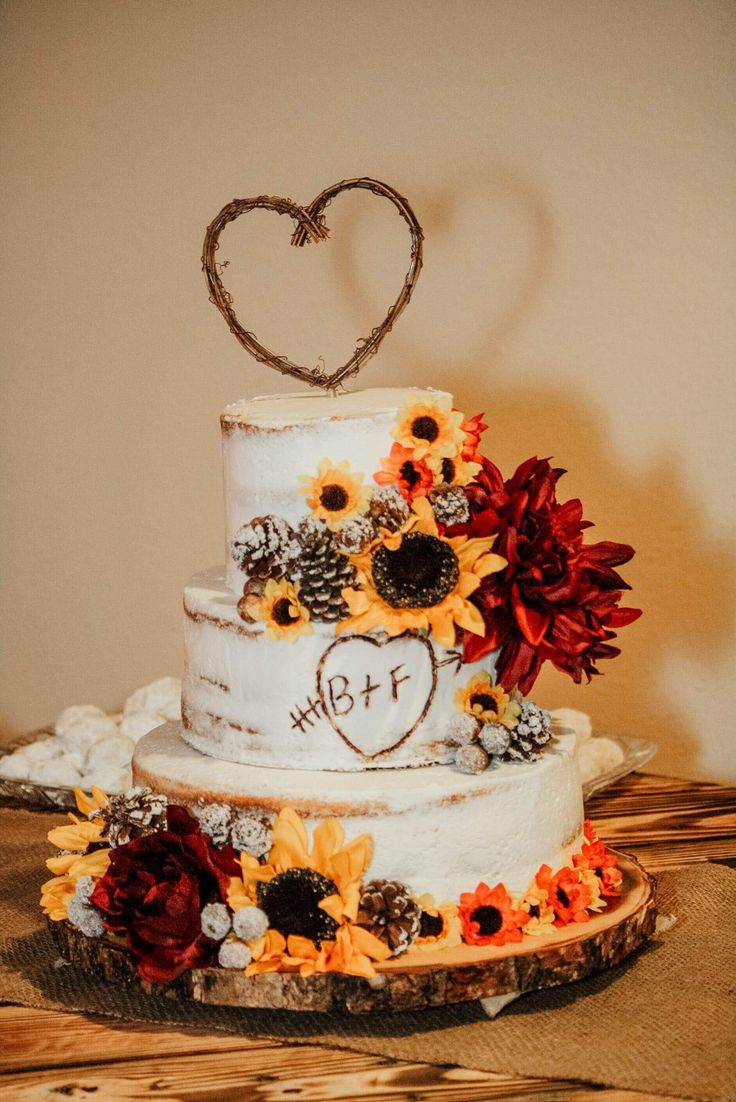 a three tiered cake with sunflowers and hearts on top is sitting on a table