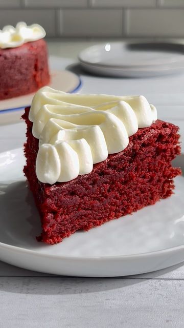 a slice of red velvet cake with white frosting on a plate next to the rest of the cake